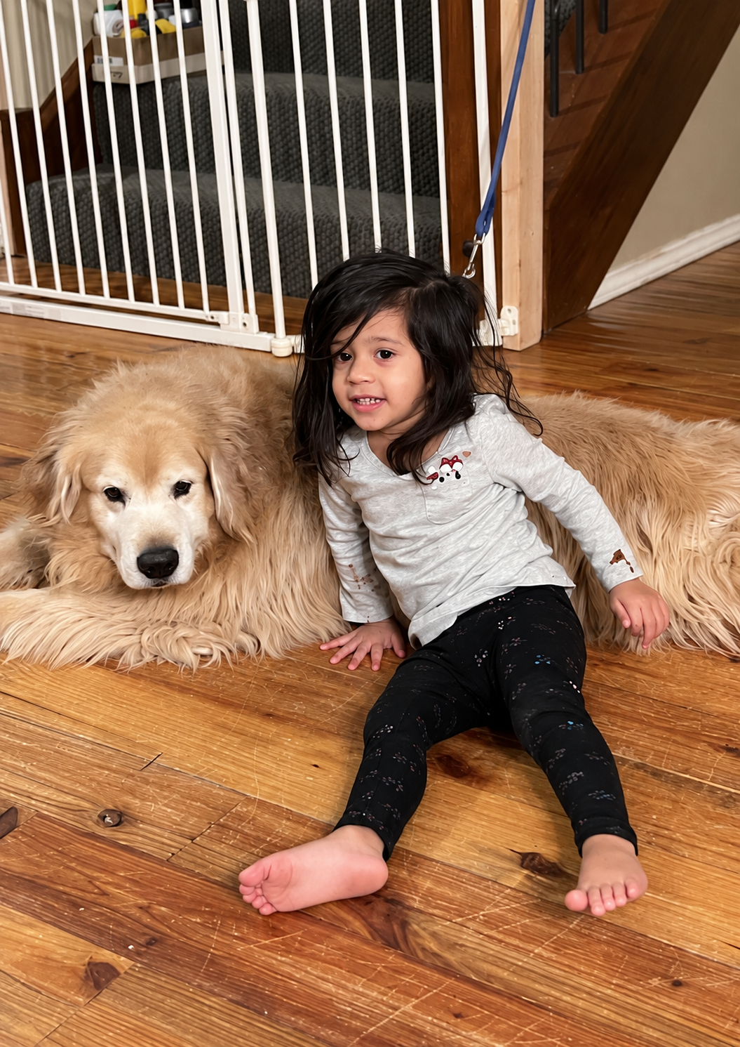 Aria sitting beside her golden retriever on the floor at home