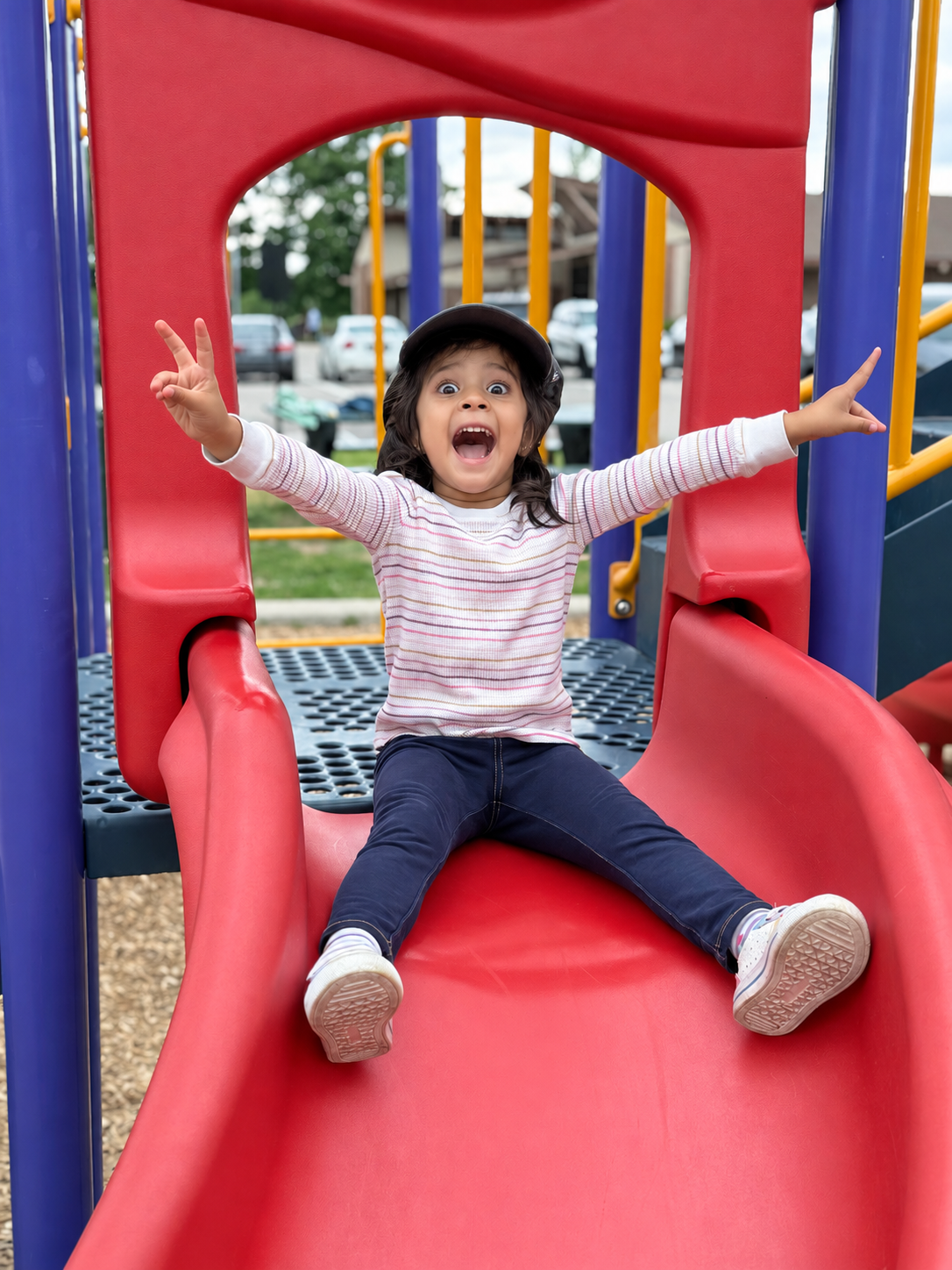 Aria beaming on a red playground slide with both arms raised