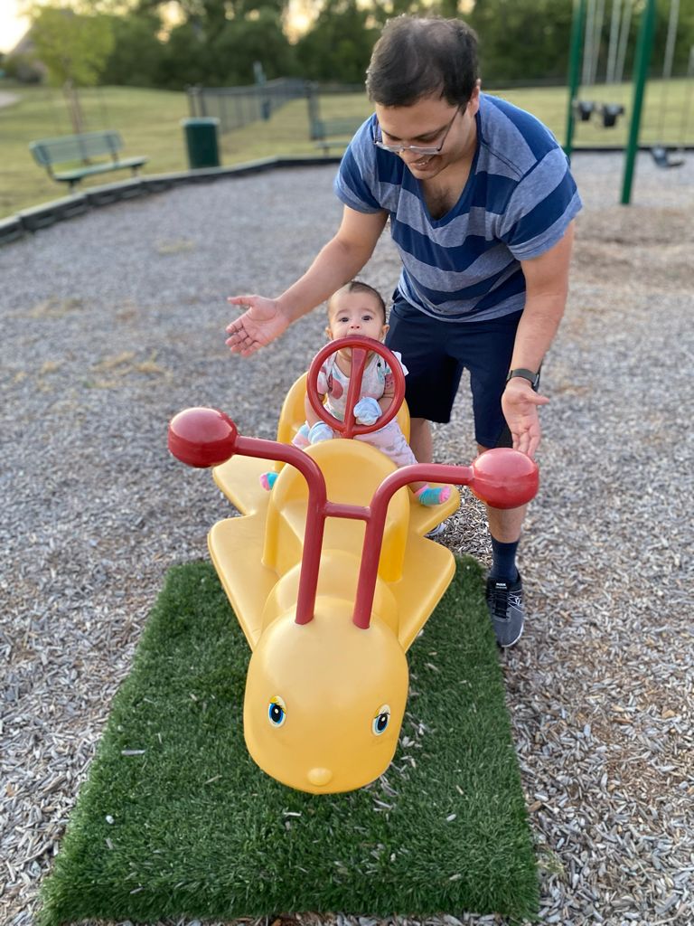 Baby Aria riding the airplane toy at the playground while Daddy steadies her