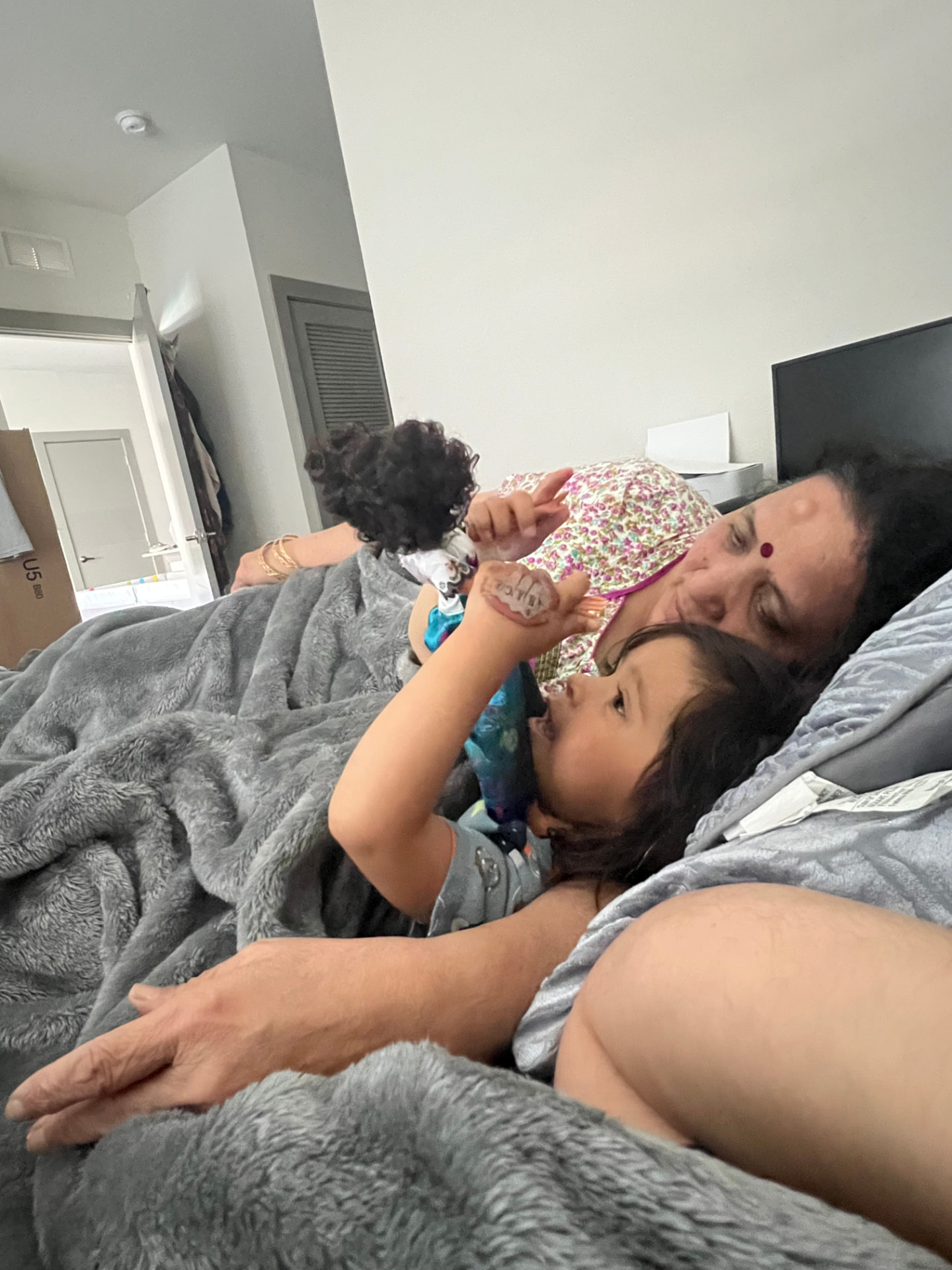 Aria snuggled in bed with her Aaji, playing with her doll