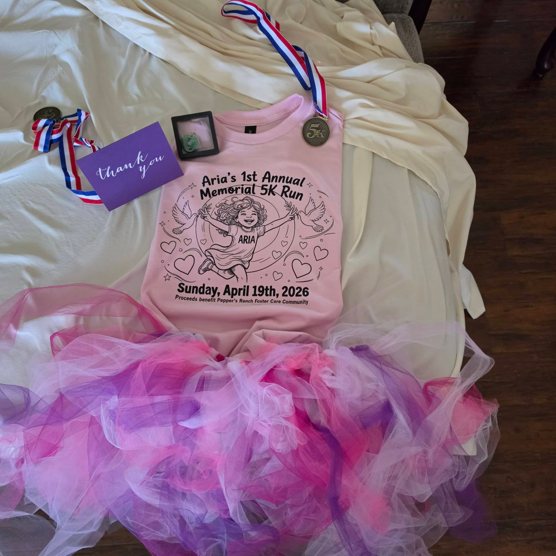 Aria's 1st Annual Memorial 5K Run shirt with medals, a thank-you card, and her pink and purple tutu