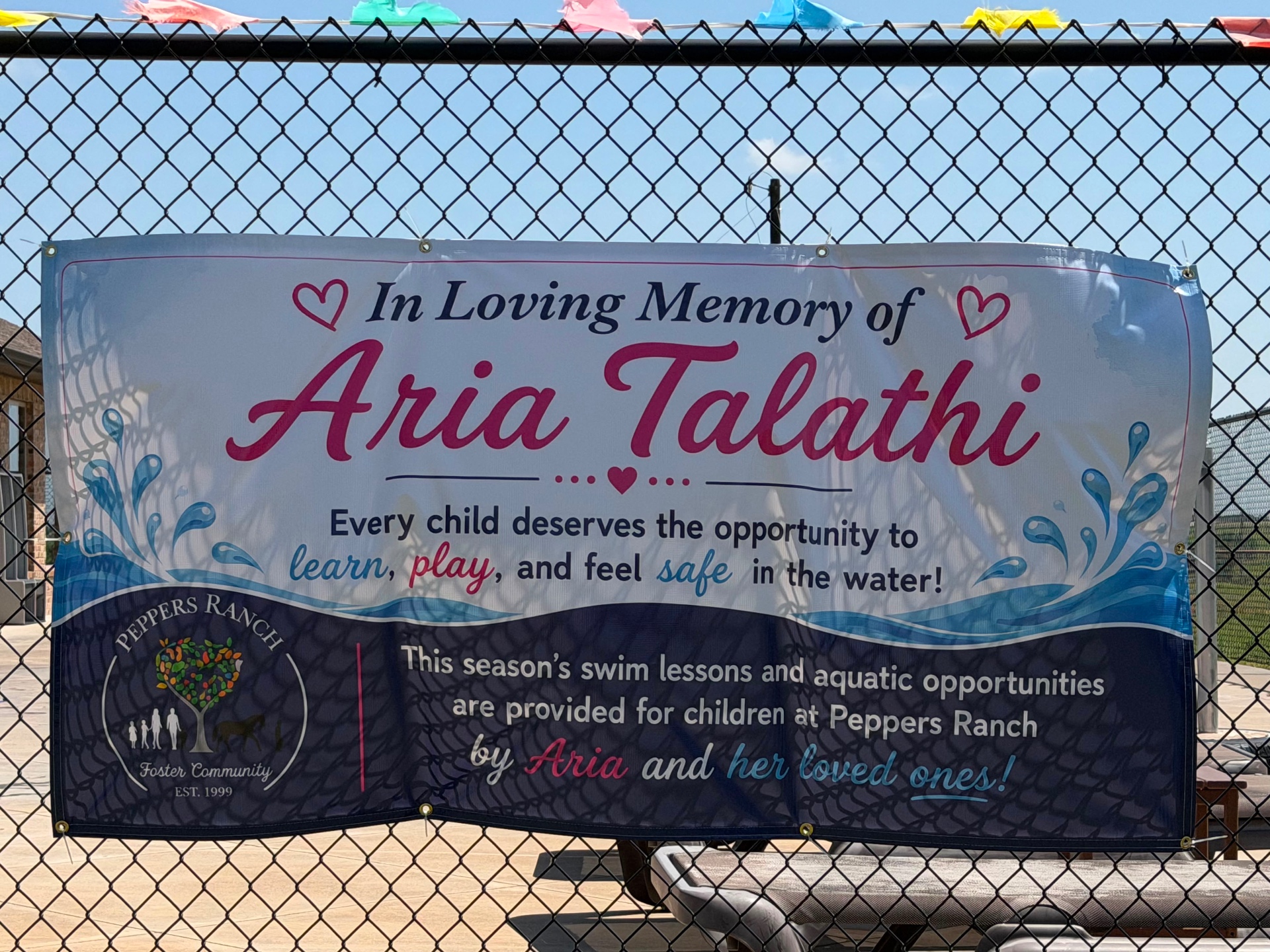 A banner by the pool at Pepper's Ranch reading: In Loving Memory of Aria Talathi — this season's swim lessons are provided by Aria and her loved ones