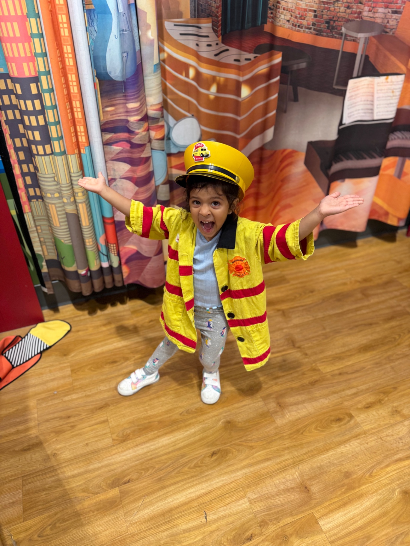 Aria dressed as a firefighter in her yellow jacket and hat, arms thrown wide