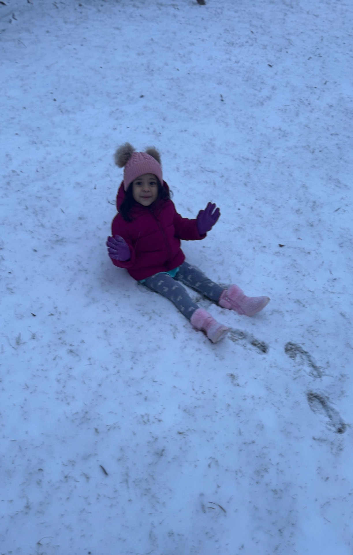 Aria bundled up in her pink hat and coat, sitting in the snow