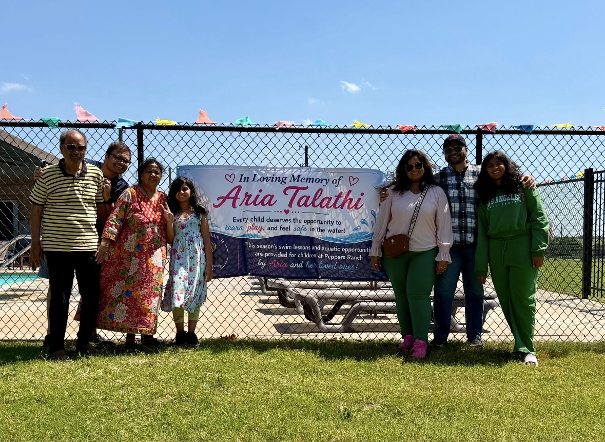 Aria's family by the pool fence in front of the Pepper's Ranch banner dedicated in her memory