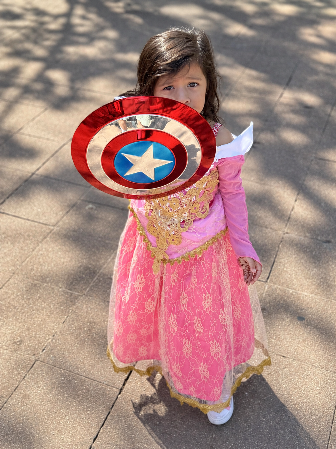 Aria in a pink princess dress holding up a superhero shield